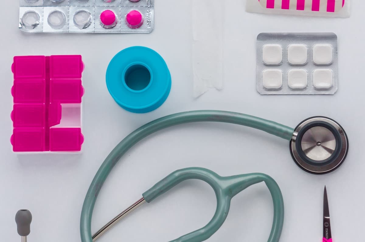 A stethoscope, pill organizer, and medical supplies laid out on a white table