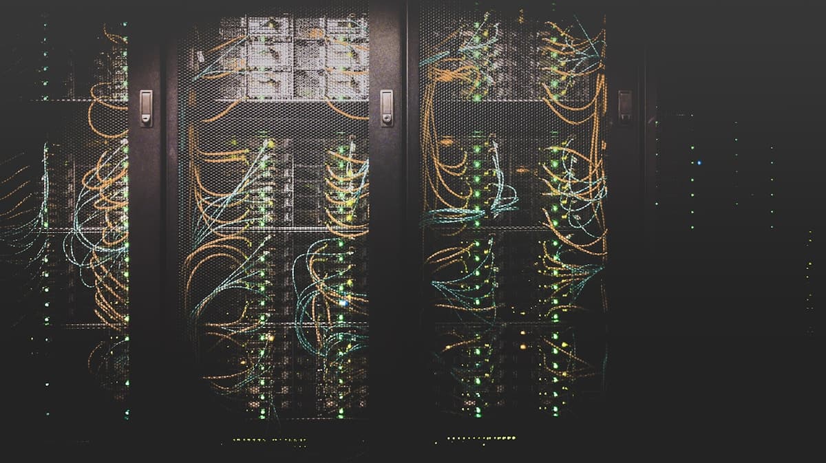 Server racks with green status lights and orange cabling behind mesh doors