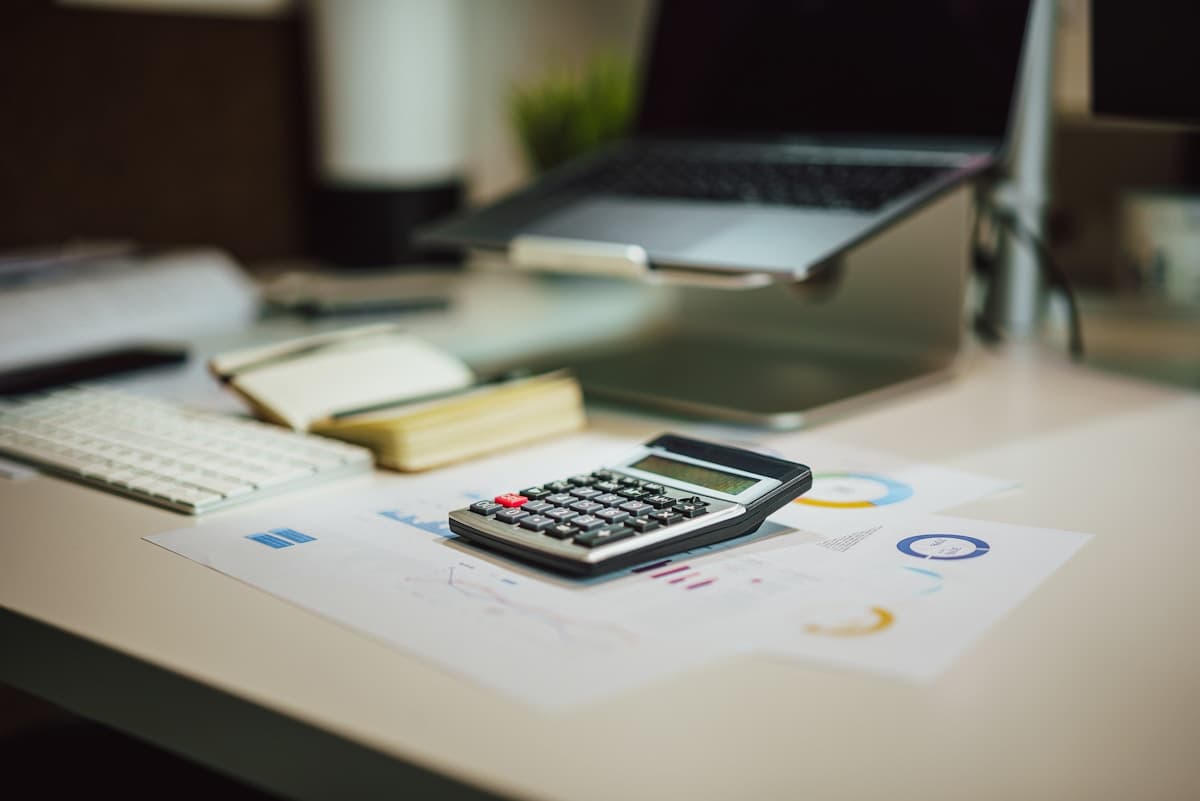A calculator resting on printed charts beside a laptop