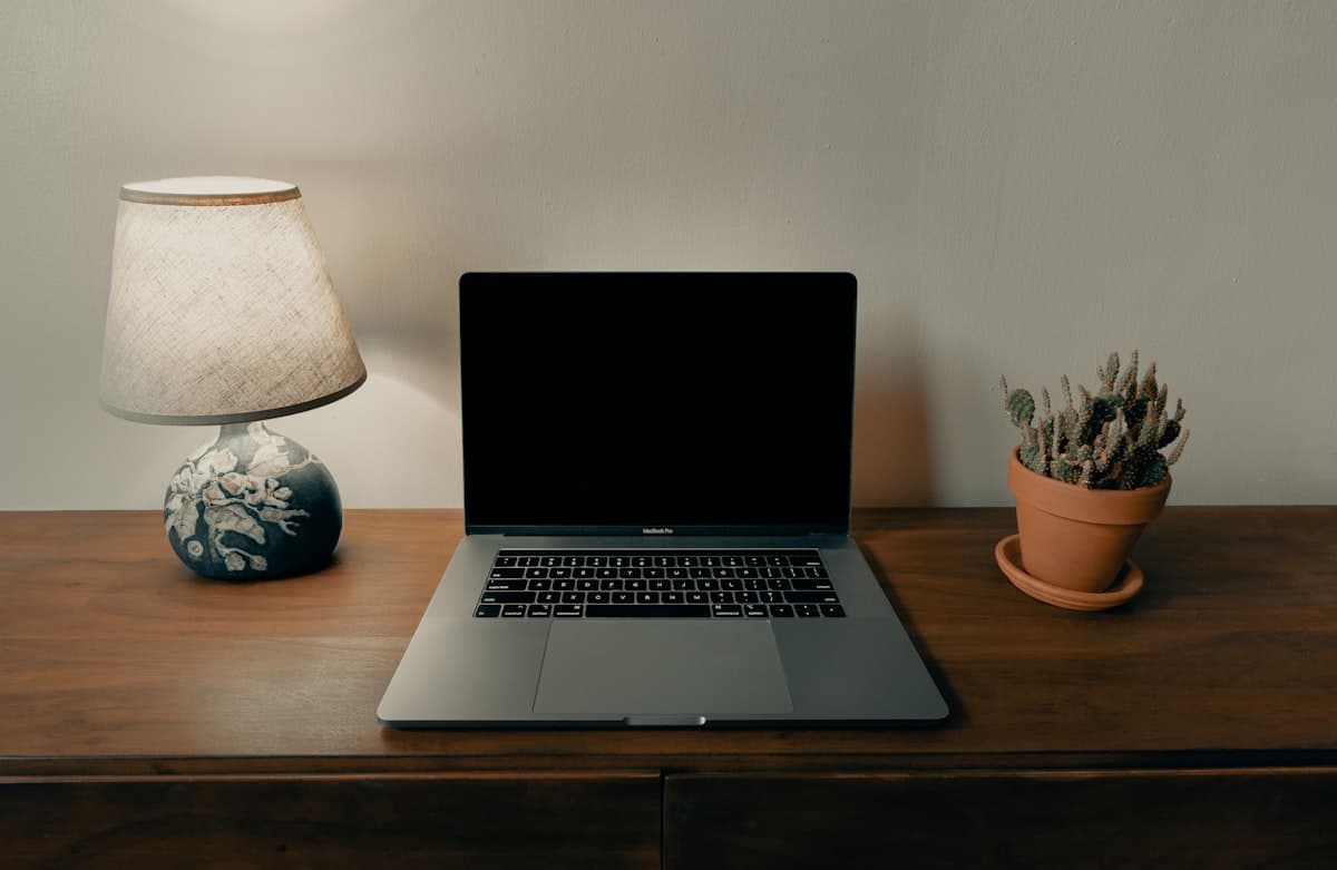 A laptop on a wooden desk at home beside a warm lamp